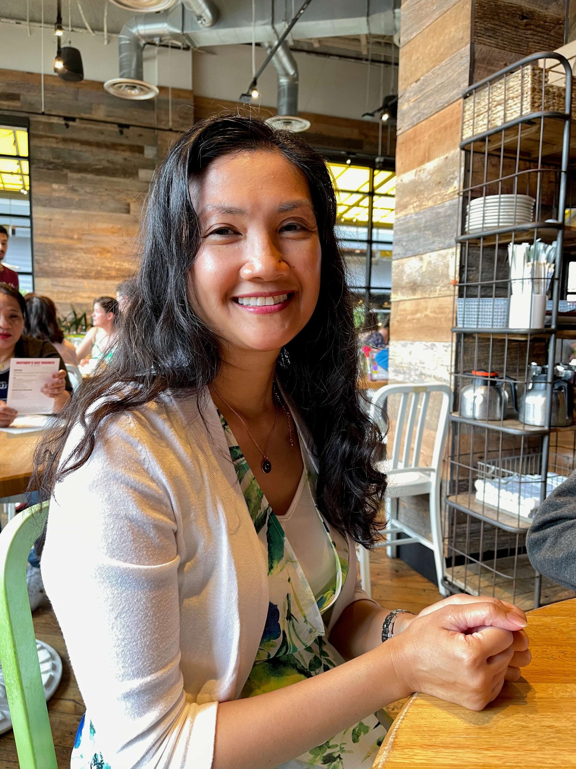 The site creator, who is a woman, sitting in a restaurant and smiling.